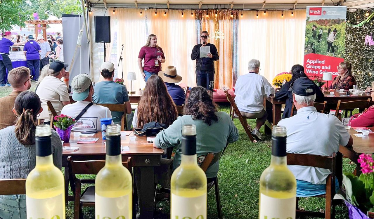 An audience of people listens to two women speaking from the front of an event at a wine festival.