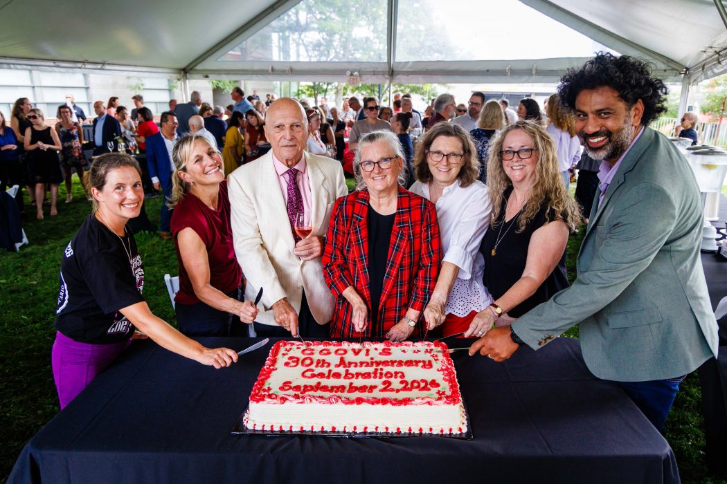 A group of people cut a large cake during an event. 