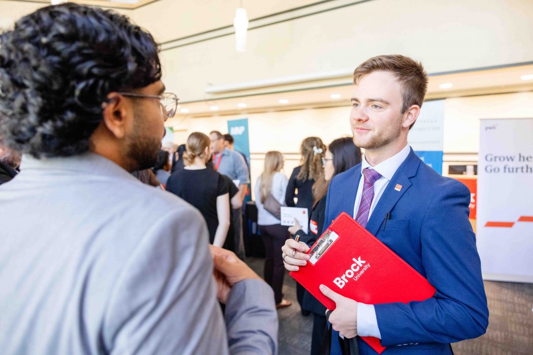 Two men in suits have a conversation at a career fair.