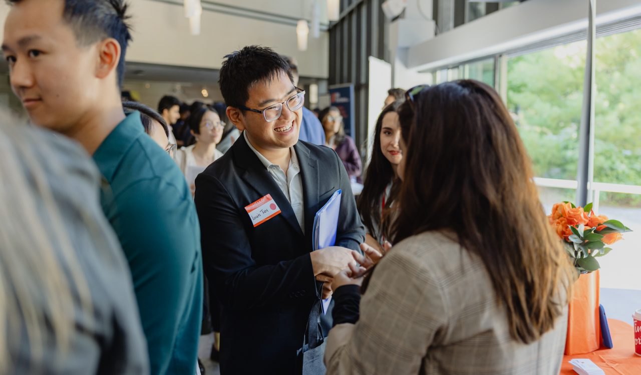 A young man in business attire speaks to a woman at a career fair.