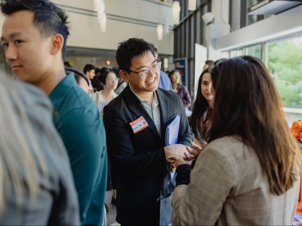 A young man in business attire speaks to a woman at a career fair.