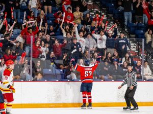 A Brock Badgers hockey player cheers while on the ice of a hockey arena, while excited fans yell back.