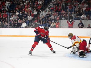 A Brock Badgers hockey player approaches a Guelph Gryphons goalie in front of a packed crowd in a hockey arena.