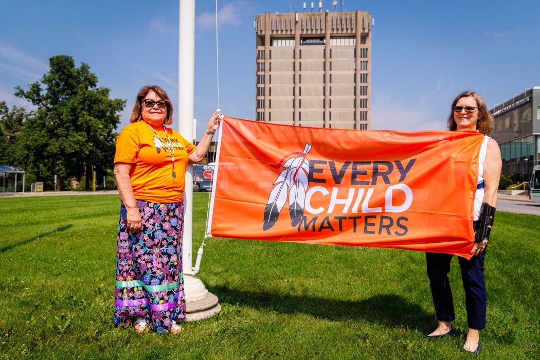 Two women hold up an orange Every Child Matters flag outside at Brock University.
