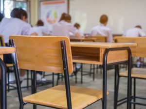 An empty chair in a classroom with students seated at desks in the background.
