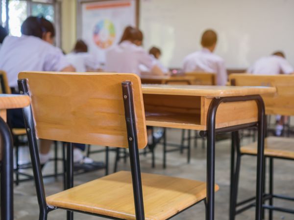 An empty chair in a classroom with students seated at desks in the background.