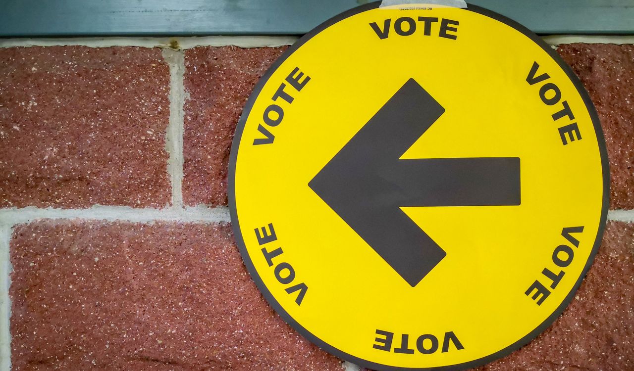 A sign hanging on a brick wall has a large arrow and says "vote" repeatedly.