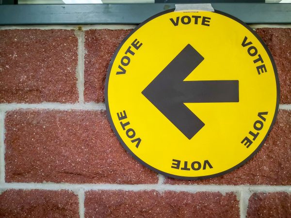 A sign hanging on a brick wall has a large arrow and says 