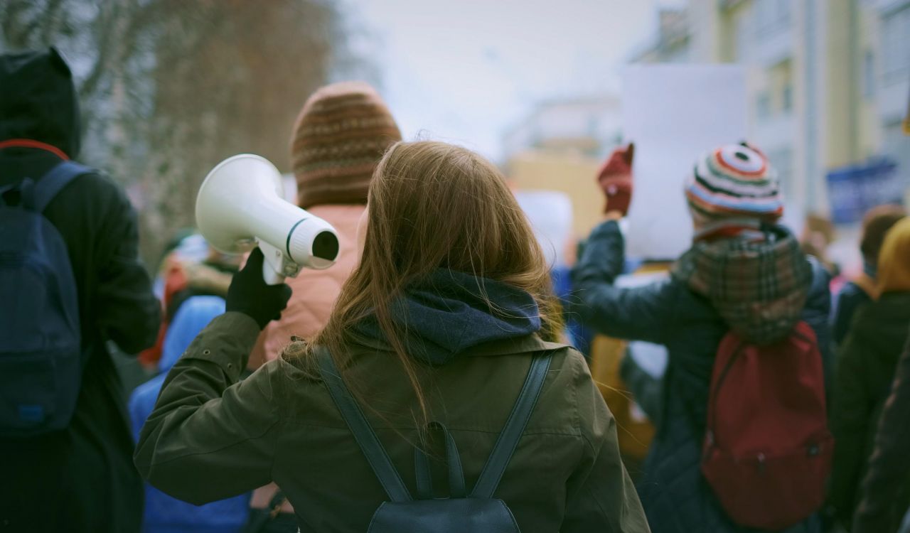 A young woman carrying a loudspeaker participates in a protest.