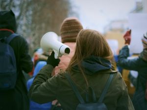 A young woman carrying a loudspeaker participates in a protest.
