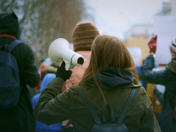 A young woman carrying a loudspeaker participates in a protest.