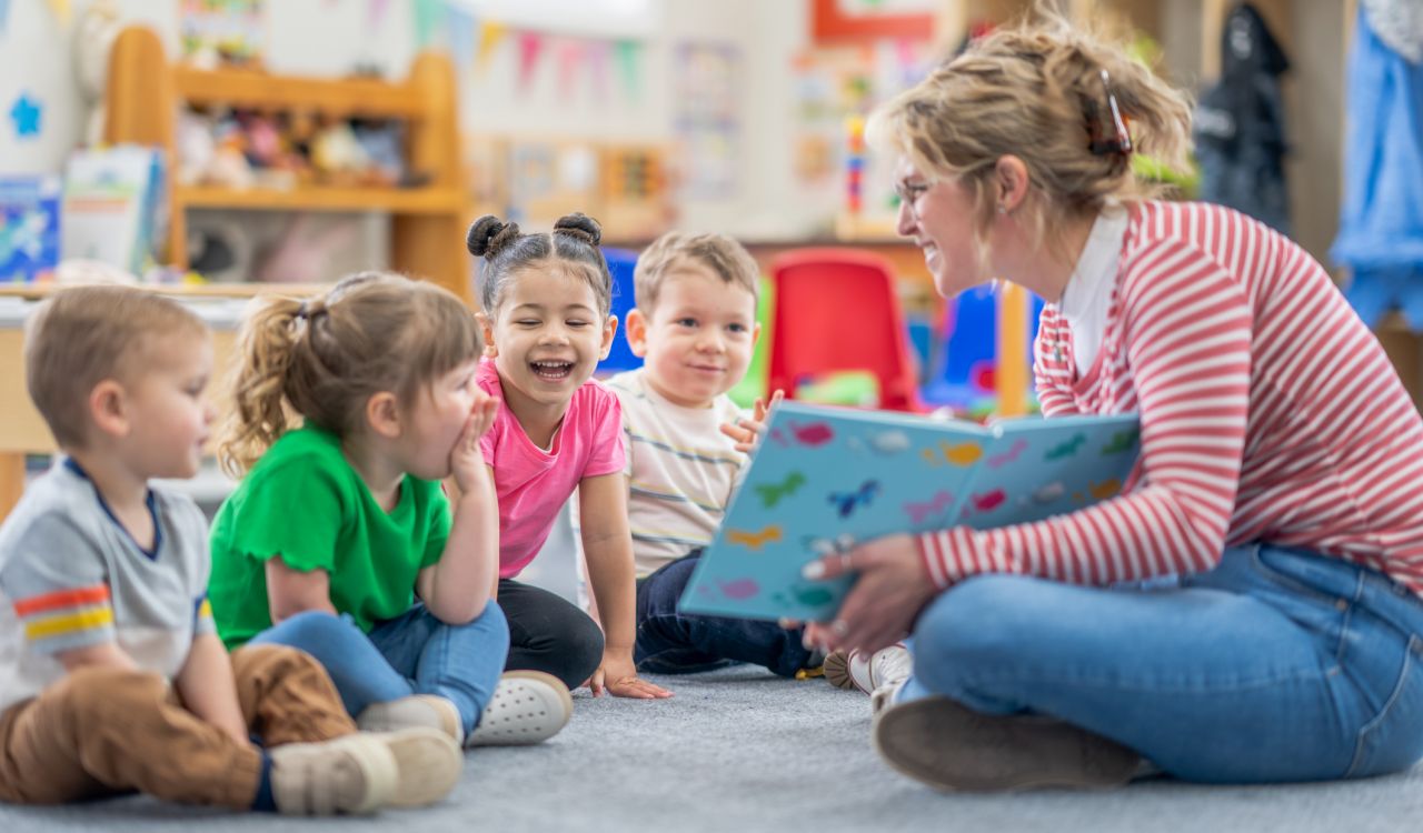 A Kindergarten teacher reads to young learners on a carpet in the classroom.