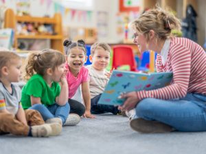 A Kindergarten teacher reads to young learners on a carpet in the classroom.