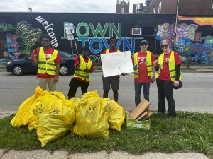 Students in red shirts and yellow vests pose with bags of garbage they collected at a volunteering event.