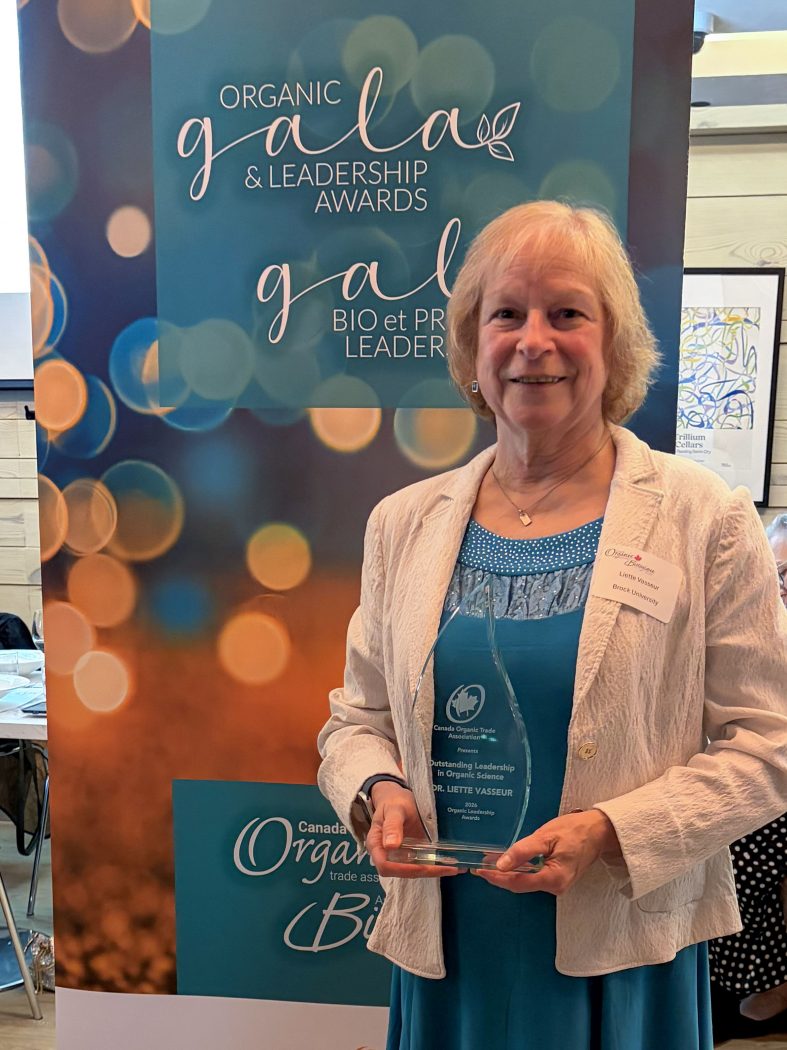 A woman poses in front of a banner holding an award.