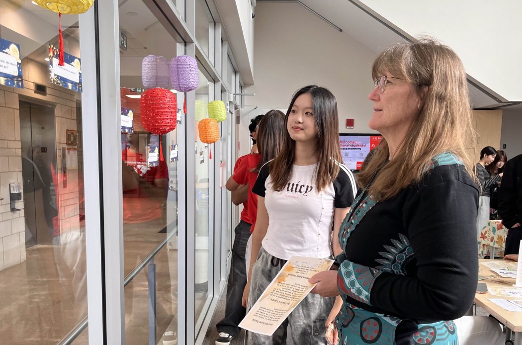 Two women look at pieces of paper taped to a window at a university event.