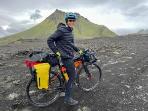 A man rests with his bicycle on a patch of flat ground with a volcano in the background.