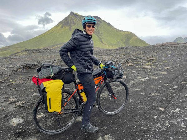 A man rests with his bicycle on a patch of flat ground with a volcano in the background.