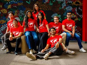 A group of young people in red shirts in front of a floral mural.