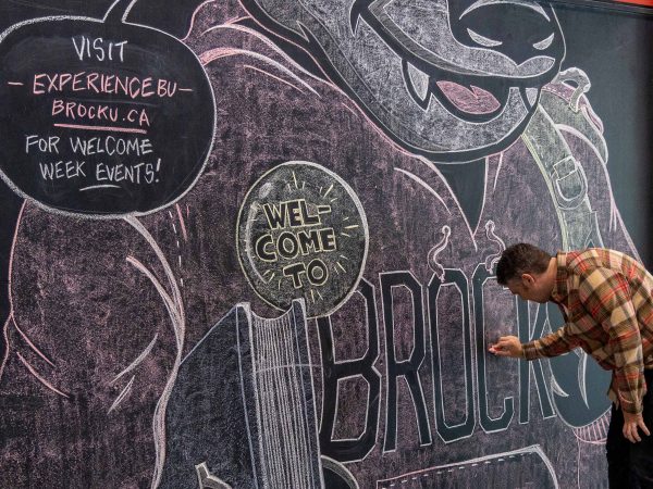 A man touches up a large chalk mural.