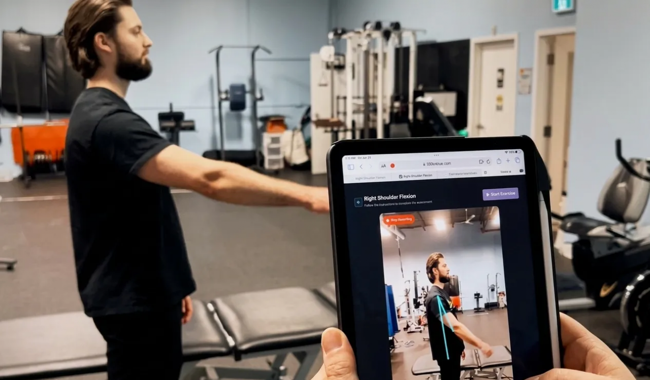 A man performs shoulder exercises while another person, holding a tablet, evaluates him.