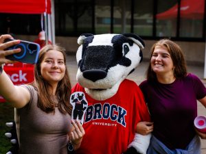 Two young women take a selfie with a Badger mascot.