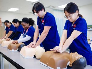 Nursing students in blue scrubs perform CPR on training manikins.