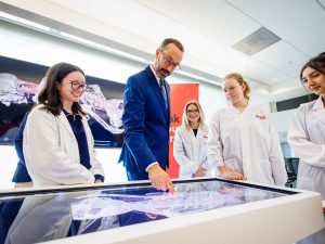 A group looks over a digital glass table featuring human anatomy.