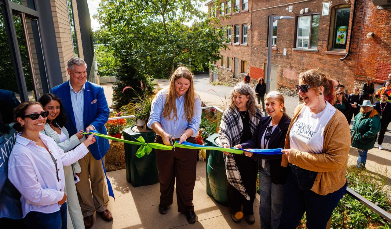 A group of people cut a green ribbon at an opening ceremony for a rain garden.