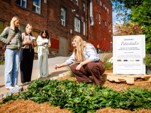 A women works in a garden while three others observe what she's doing.