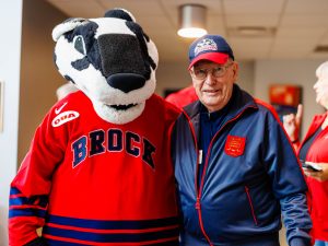 An older man poses with Boomer the Badger, Brock University's mascot.