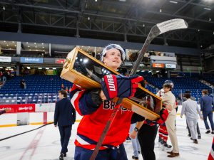 A Brock Badgers hockey player holds a trophy while on the ice of an arena.