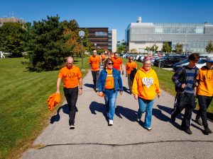 A group of people wearing orange shirts walk together outdoors on the Brock campus,
