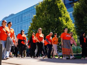 A group of people wearing orange shirts walk together outdoors on the Brock campus,