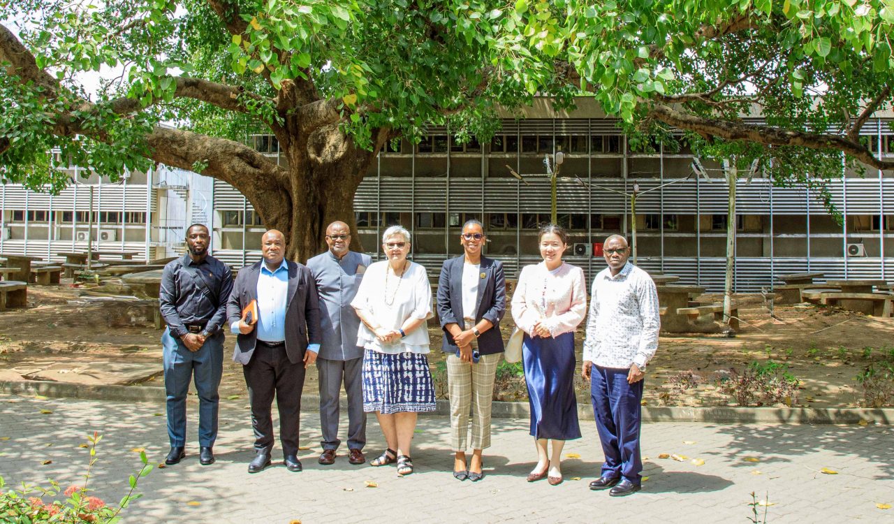 A group of people pose for a photo under a large tree on a university campus.