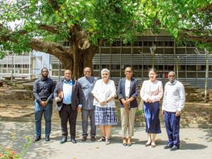 A group of people pose for a photo under a large tree on a university campus.