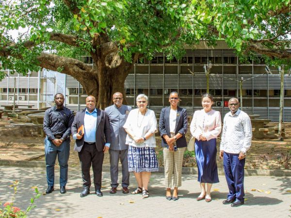 A group of people pose for a photo under a large tree on a university campus.