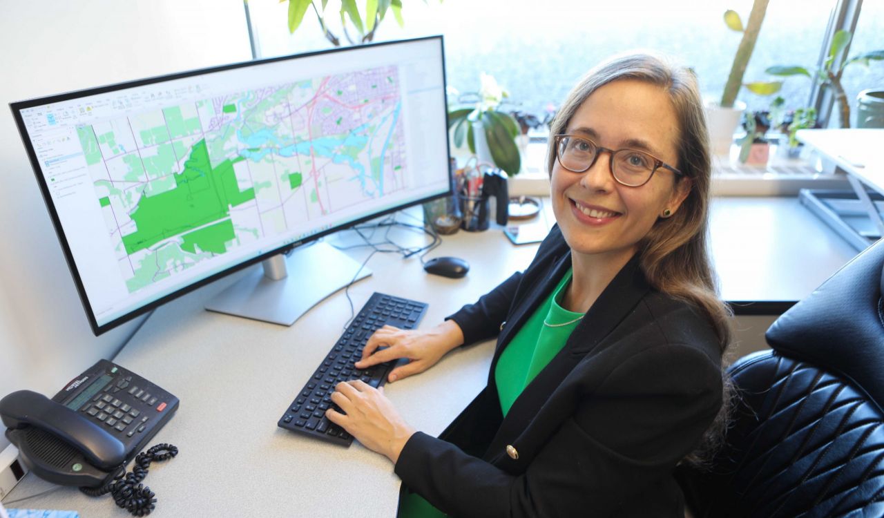 Samantha Hajna sits at her desk, with a large screen displaying a map and her hands on a keyboard.