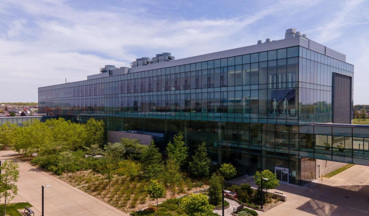 A glass building surrounded by gardens on a sunny day.
