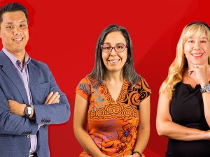 Three people stand together against a red backdrop.