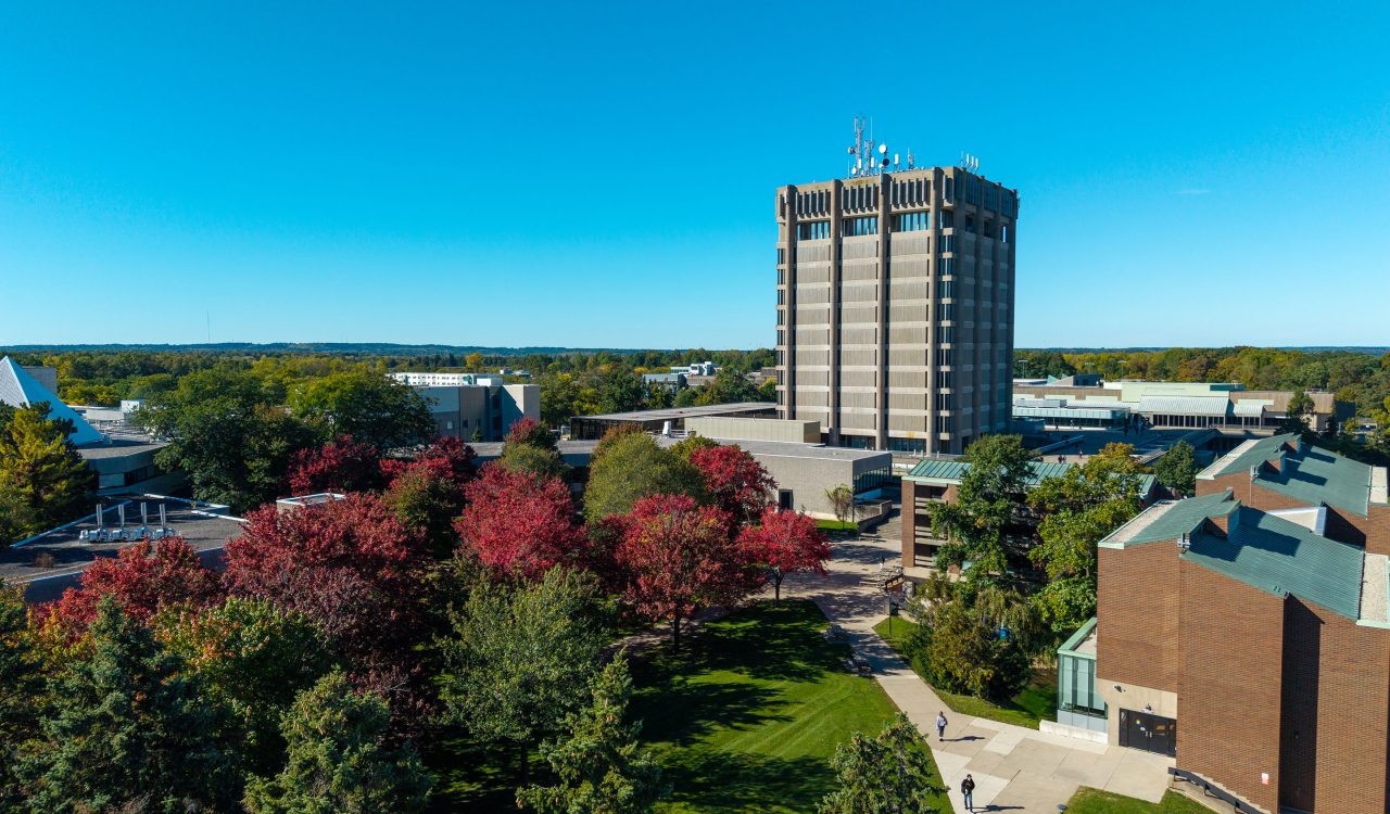 A large concrete tower stands at the heart of a university campus with fall foliage and colourful leaves lining a variety of buildings.