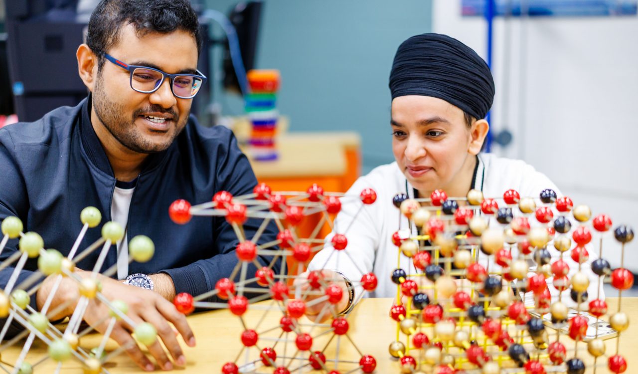 Two people sit together at a table looking over colourful balls and sticks put together to create molecule models.