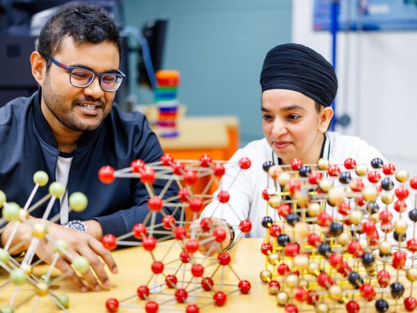 Two people sit together at a table looking over colourful balls and sticks put together to create molecule models.