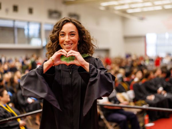 Alyssa Scalera smiles, wearing a black graduation robe with a green hood on stage at Fall Convocation held inside the Ian D. Beddis Gymnasium at Brock University.