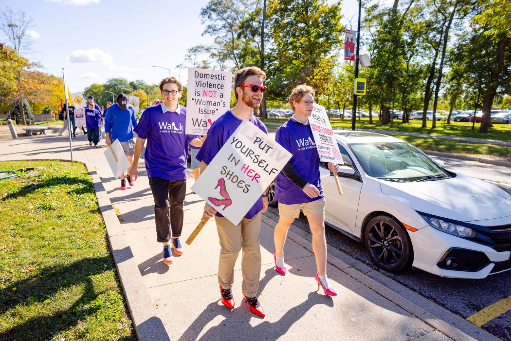 Young men wearing heels carry signs protesting violence against women.