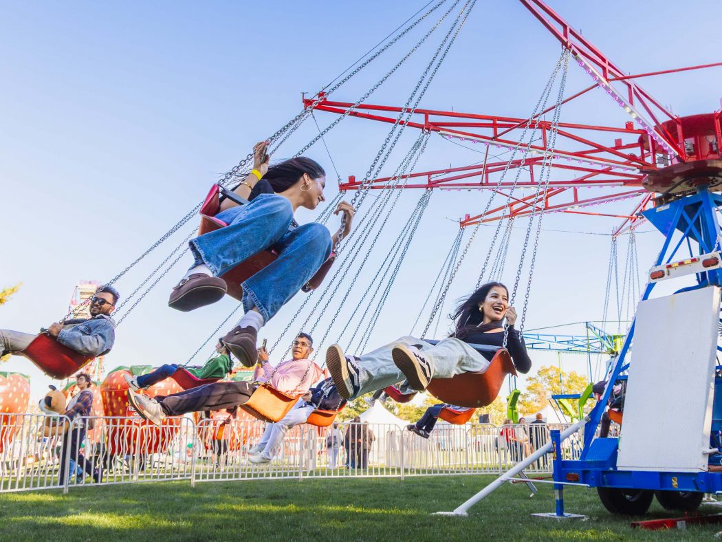 University students on a swing ride at a carnival on a sunny day.
