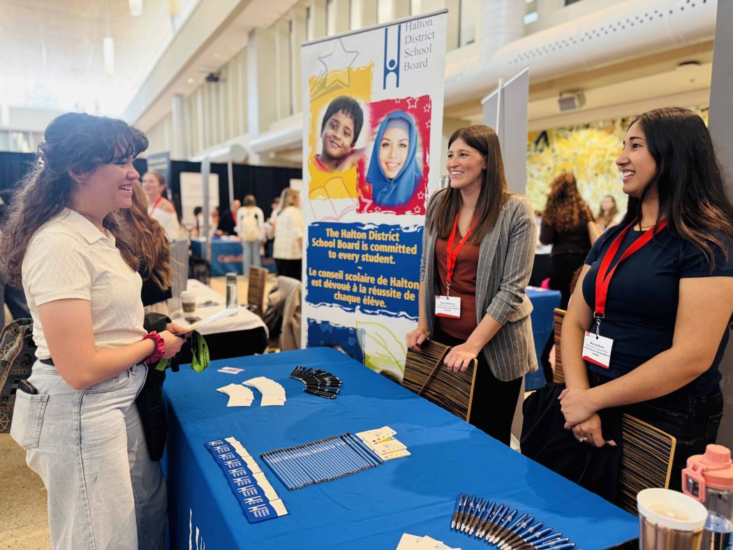 Three people stand and have a conversation at a career fair booth.