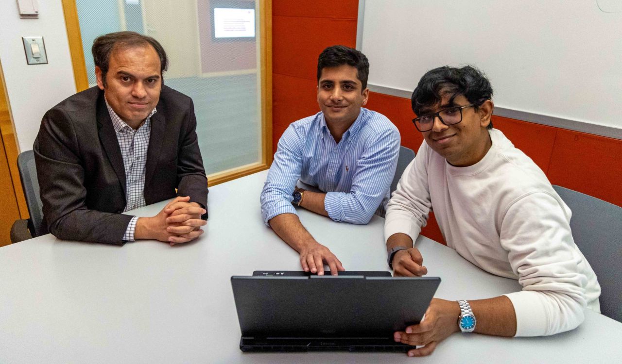 Naser Ezzati-Jivan, Yuvraj Sehgal and Sneh Patel sit at a table in front of a laptop, smiling and looking up into the camera.