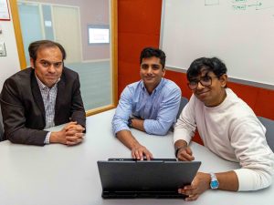 Naser Ezzati-Jivan, Yuvraj Sehgal and Sneh Patel sit at a table in front of a laptop, smiling and looking up into the camera.