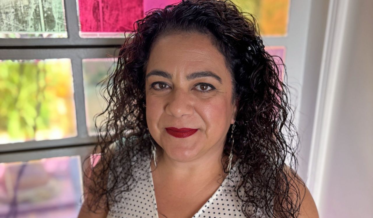 Brock professor Cristina Santos smiles in front of a colourful window.